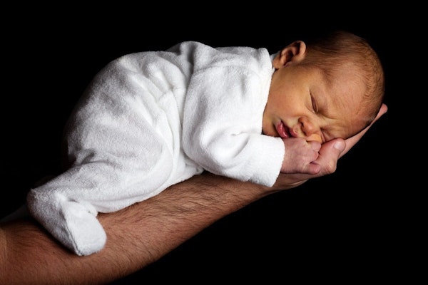 Ein Neugeborenes in weissem Strampler auf einem Arm.