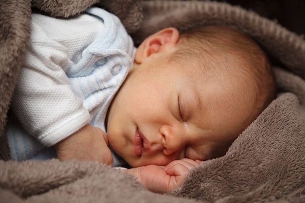 Ein Baby in weissem Hemd liegt in eine braune Decke eingewickelt und schläft